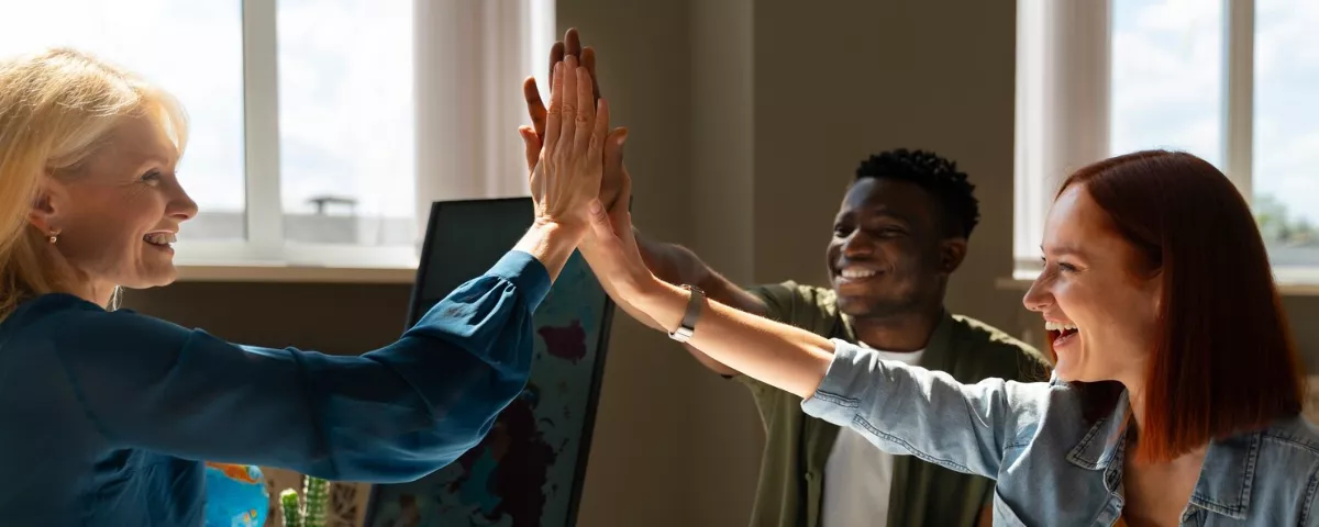 Équipe de collaborateurs faisant un high-five au bureau pour célébrer la constitution d'une équipe soudée.