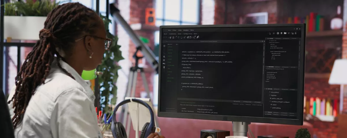 Développeuse femme avec dreadlocks travaillant sur du code informatique sur grand écran.