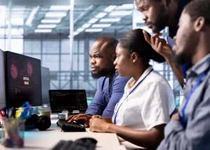 Professionnels de l'IT en réunion de travail devant un écran affichant un code source au sein d'un centre de services externalisés.