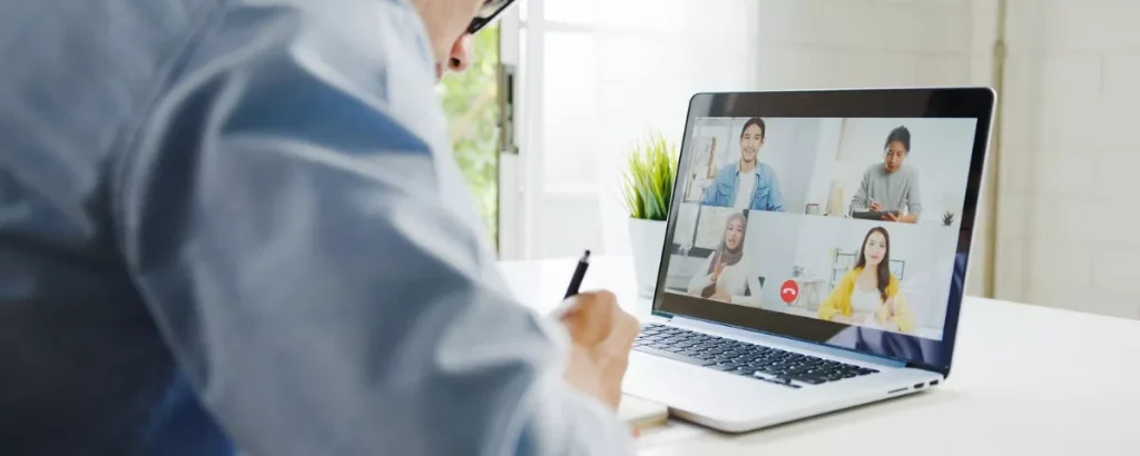 Travail hybride et communication à distance : cadre supérieur en réunion vidéo avec 4 collaborateurs, notant des idées.