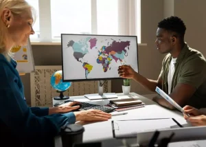 Équipe de gestion RH échangeant autour d'un écran affichant une carte du monde lors de la sélection d'un EOR à Madagascar pour l'externalisation de talents.